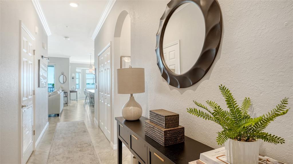 A hallway features a dark console table with a lamp, mirror, and plant, leading toward a living area — 910 TIDEWATER SHORES LOOP UNIT 402, BRADENTON, FL