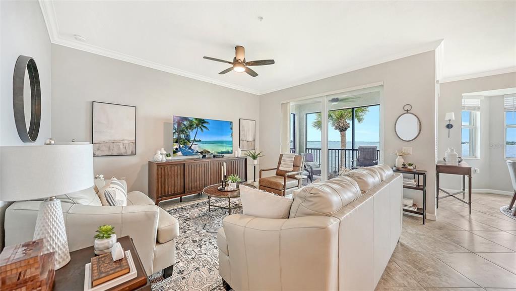 A living room features light-colored leather sofas, a wooden media console, and a waterfront balcony — 910 TIDEWATER SHORES LOOP UNIT 402, BRADENTON, FL