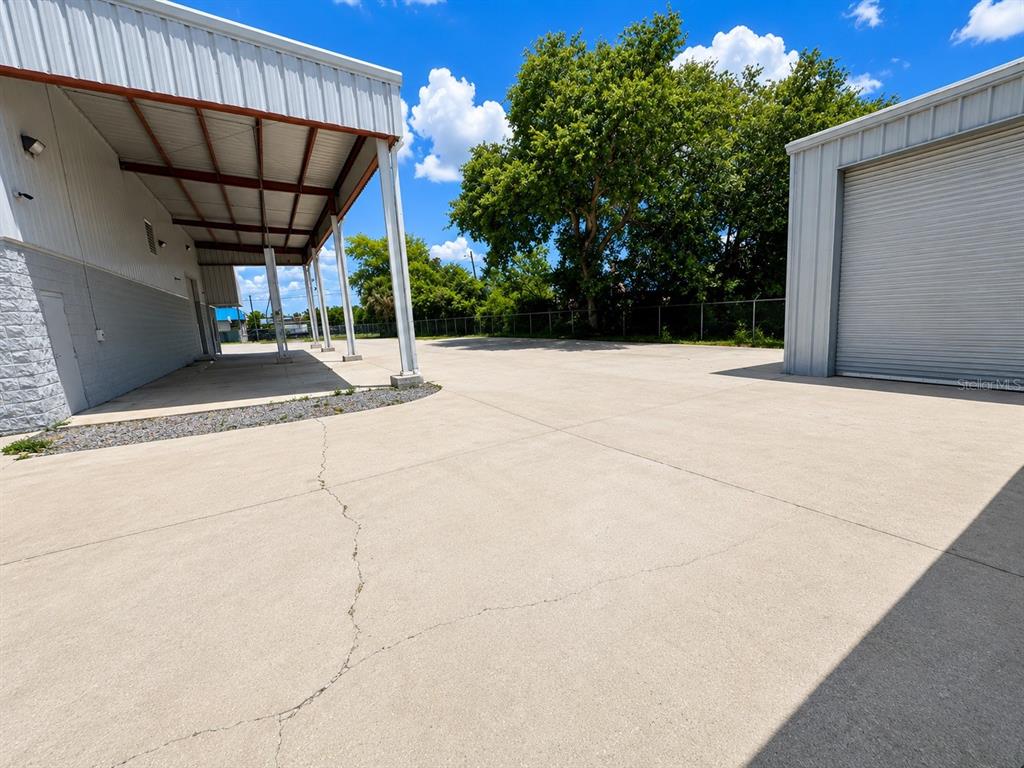 A concrete parking area sits between two metal industrial buildings under a blue sky — 5909 ANNO AVENUE, ORLANDO, FL