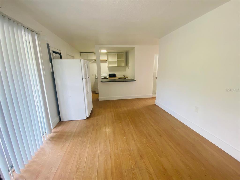 A kitchen with white appliances and wood-look flooring opens into a living area — 1341 WEST POINT DRIVE UNIT 07, COCOA, FL