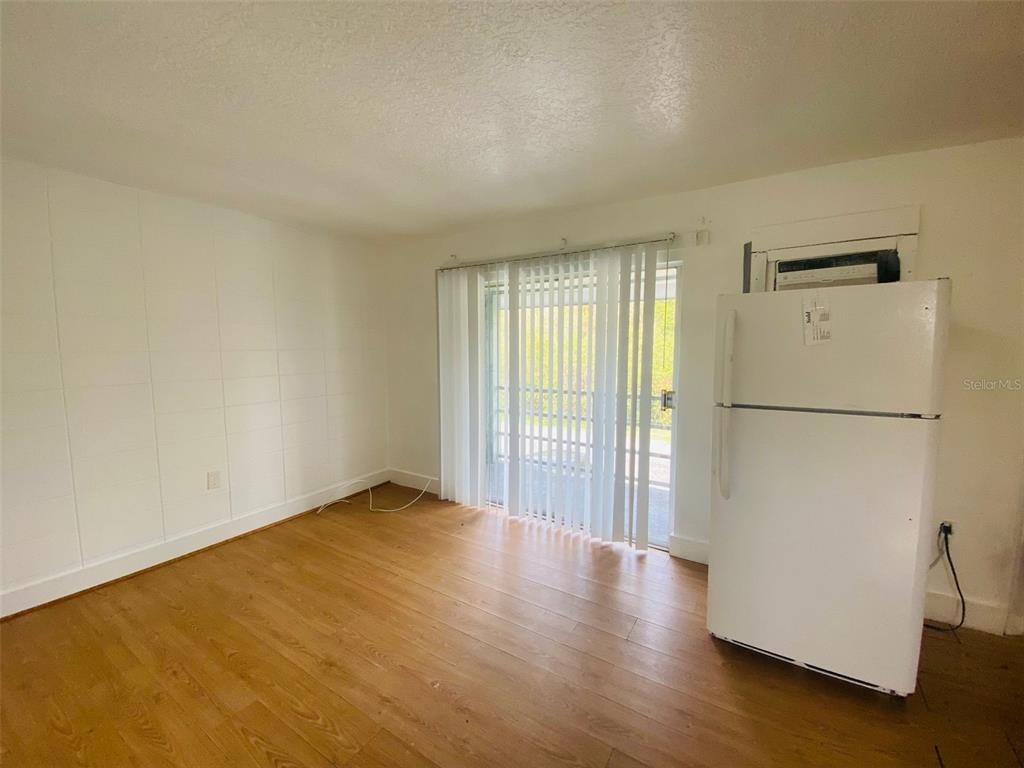 A room with light wood-look flooring, white walls, a sliding glass door, and a refrigerator — 1341 WEST POINT DRIVE UNIT 07, COCOA, FL