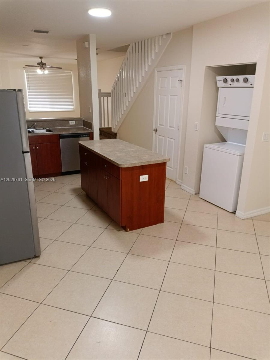 A kitchen features a central island, tile flooring, and a stacked washer and dryer unit — 1936 Alamanda Way # 1, Riviera Beach FL 33404, RIVIERA BEACH, FL