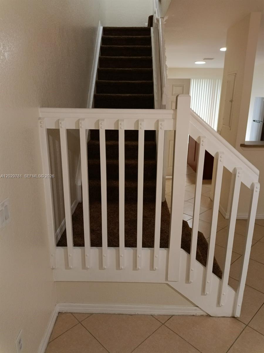A carpeted staircase features a white wooden railing and balusters in a tiled entryway — 1936 Alamanda Way # 1, Riviera Beach FL 33404, RIVIERA BEACH, FL