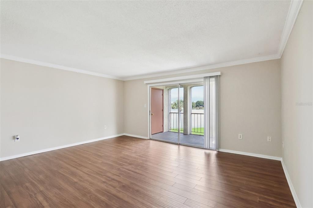 An empty living room with wood-look flooring, beige walls, and a sliding glass door to a balcony — 534 ORANGE DRIVE UNIT 27, ALTAMONTE SPRINGS, FL