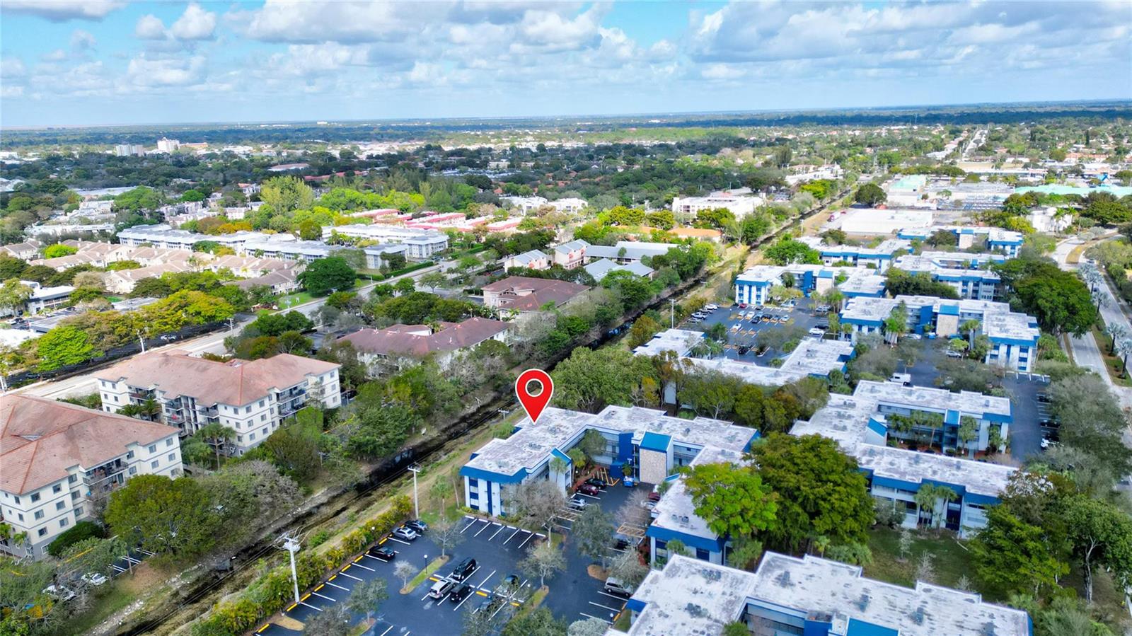An aerial view shows a multi-story apartment complex with a parking lot and surrounding greenery — 3150 Holiday Springs Boulevard # 311, Margate FL 33063, MARGATE, FL