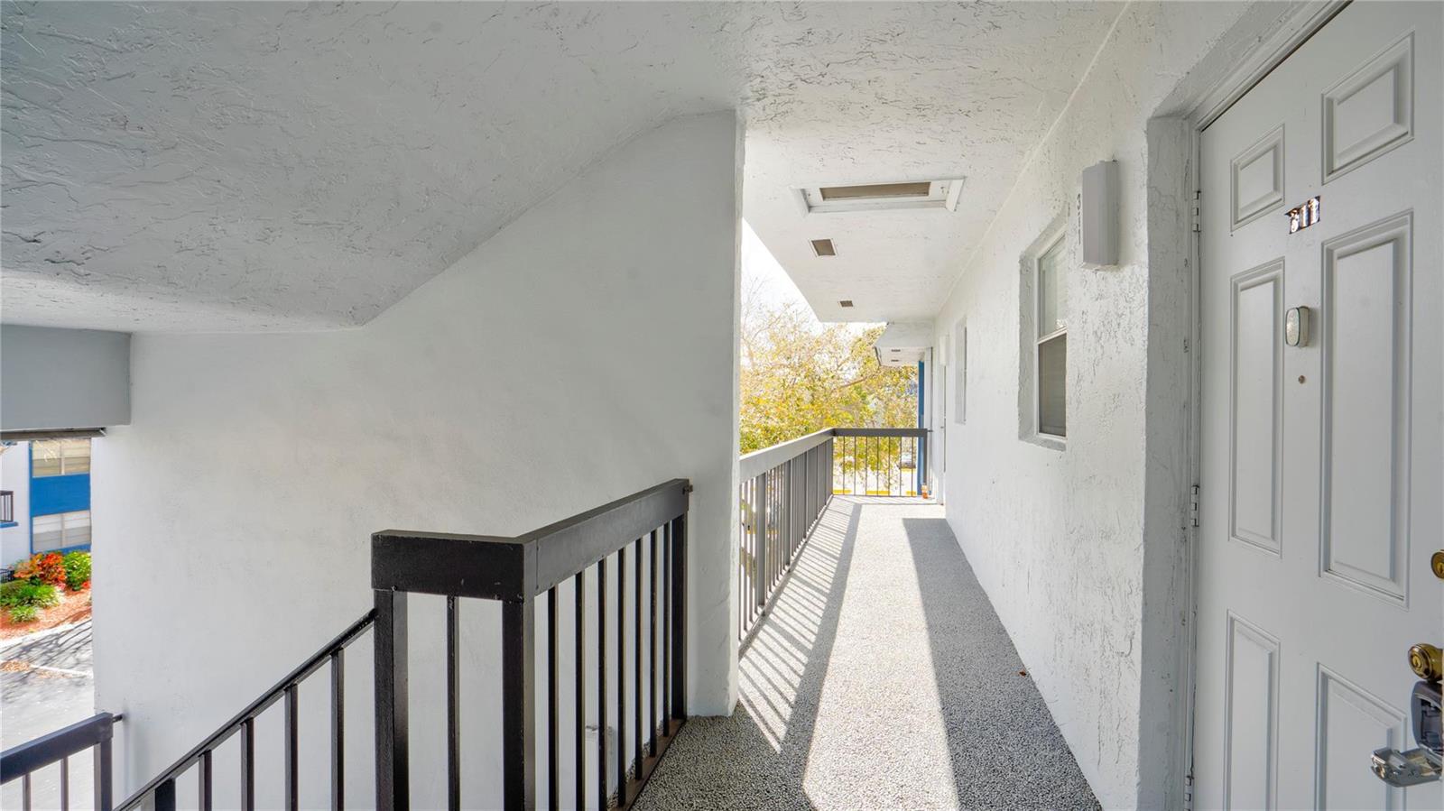 An outdoor apartment walkway features a white door, black metal railings, and textured concrete flooring — 3150 Holiday Springs Boulevard # 311, Margate FL 33063, MARGATE, FL