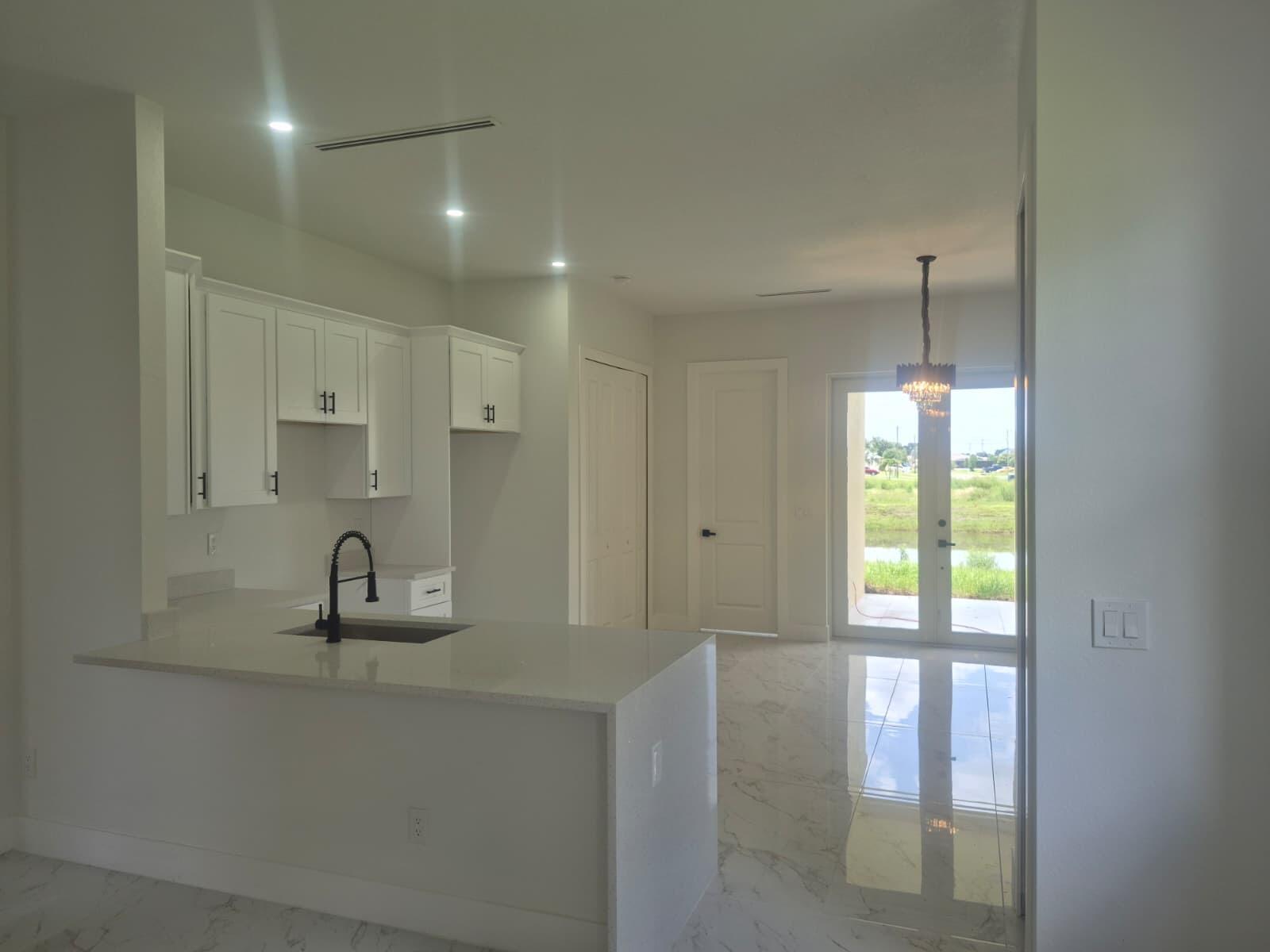 A modern kitchen with white cabinets, quartz countertops, and marble-look tile flooring overlooks a backyard — 546 Pachman Circle, Lehigh Acres FL 33974, LEHIGH ACRES, FL