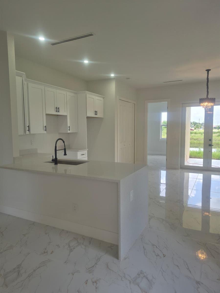 A kitchen with white cabinets, quartz countertops, and marble-look tile flooring overlooks a living area — 546 Pachman Circle, Lehigh Acres FL 33974, LEHIGH ACRES, FL