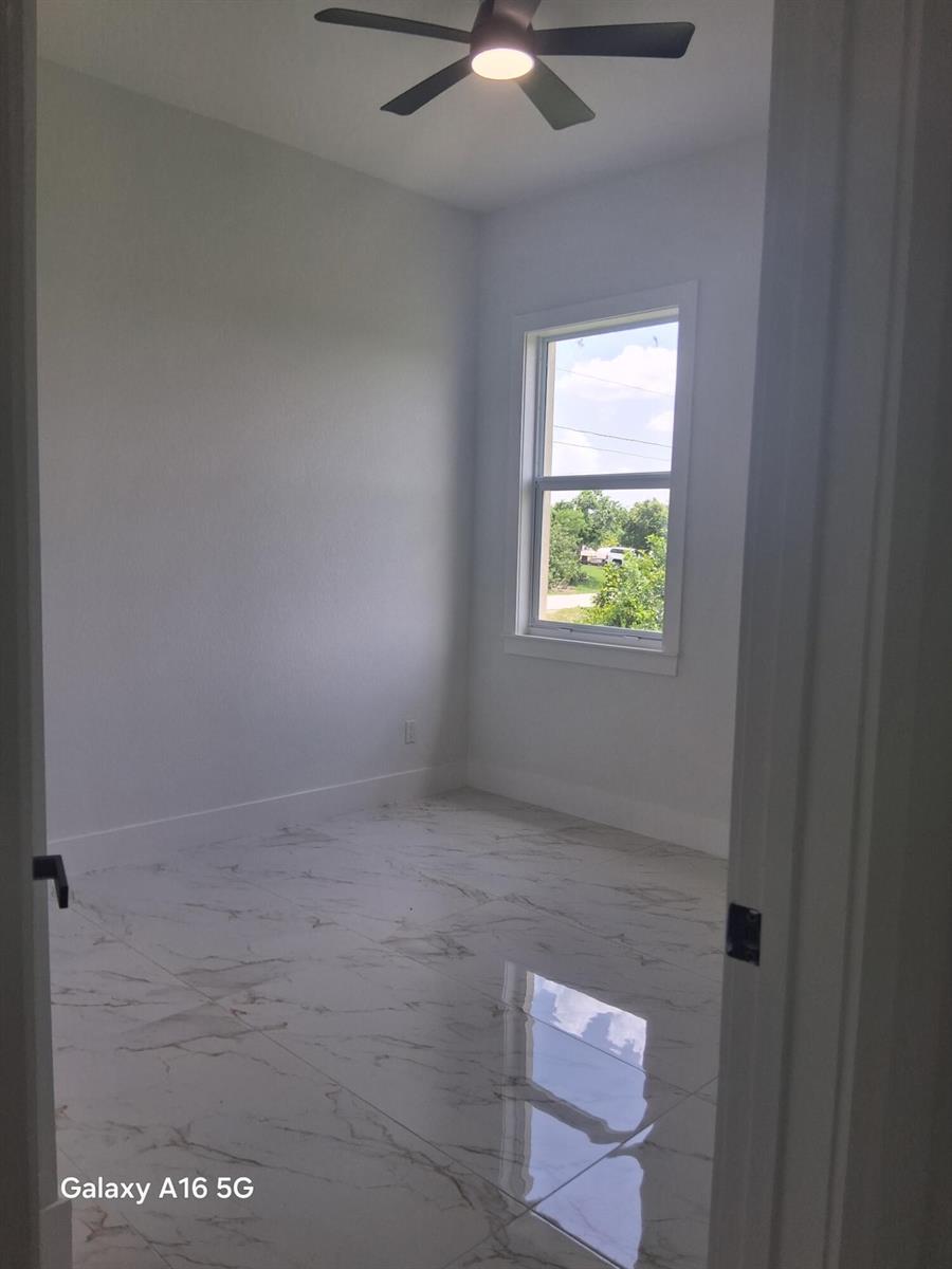 An empty room features white walls, a ceiling fan, and polished white marble-patterned tile flooring — 546 Pachman Circle, Lehigh Acres FL 33974, LEHIGH ACRES, FL