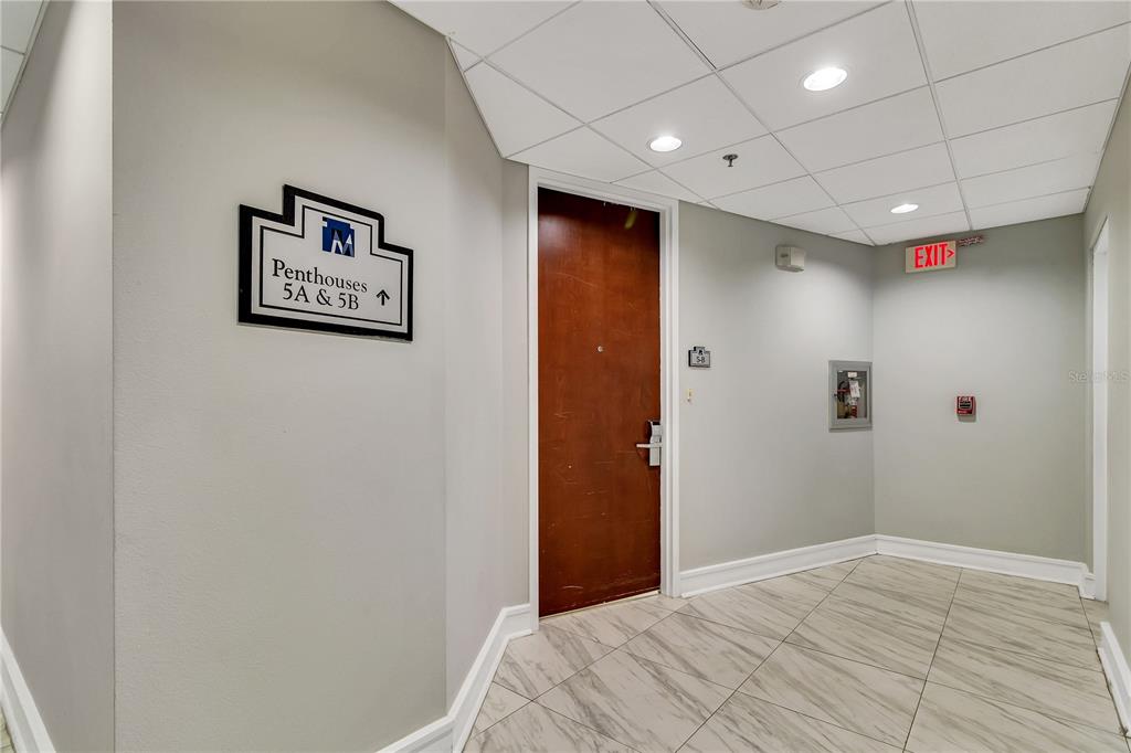A hallway with a wooden door, a directional sign for penthouses, and tiled flooring — 151 E WASHINGTON STREET UNIT 5B, ORLANDO, FL