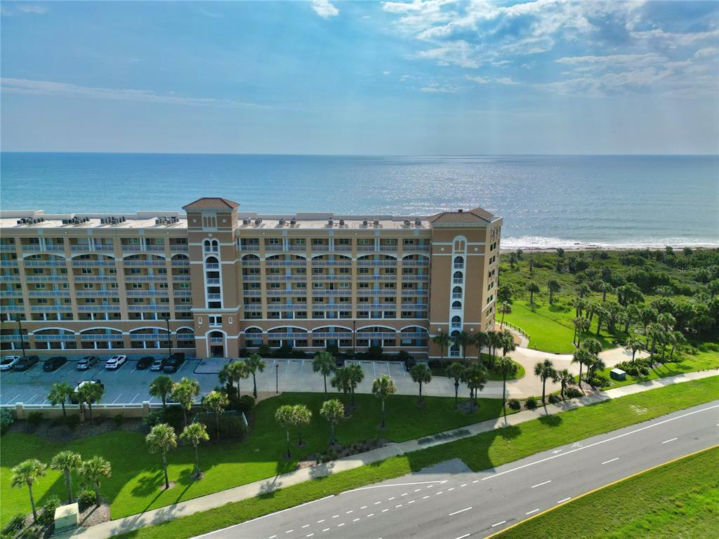 An aerial view shows a multi-story beachfront resort building with a parking lot and road — 60 SURFVIEW DRIVE UNIT 421, PALM COAST, FL