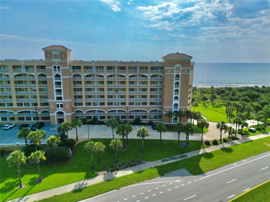 An aerial view of a multi-story tan beachfront condominium building with a parking lot — 60 SURFVIEW DRIVE UNIT 421, PALM COAST, FL
