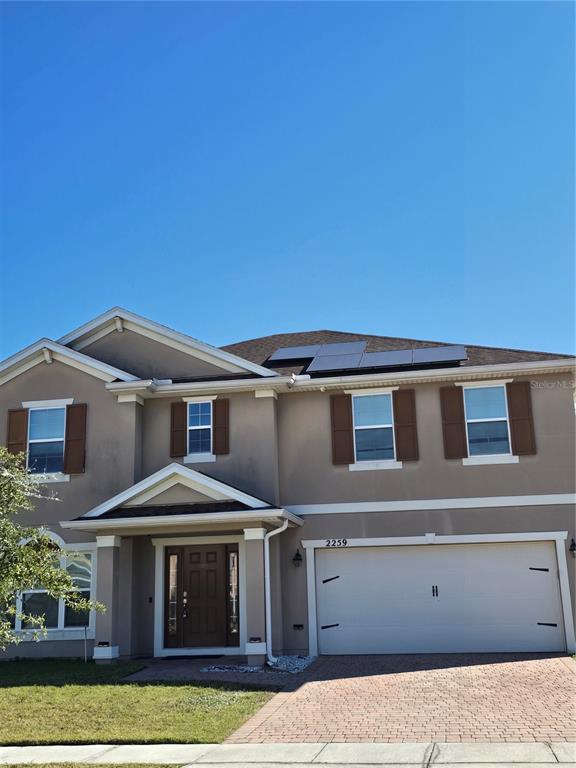 A two-story house with a beige stucco exterior, brown shutters, and solar panels on the roof — 2259 WAUKEGAN DRIVE, KISSIMMEE, FL