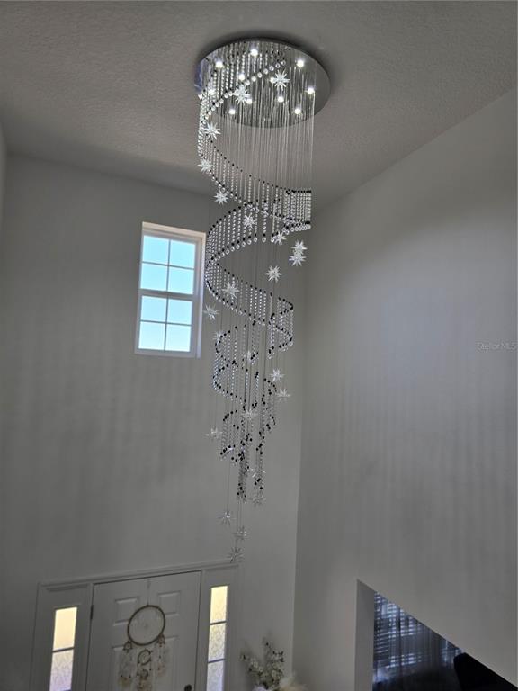 A tall spiral crystal chandelier hangs in a bright, high-ceilinged entryway with a front door — 2259 WAUKEGAN DRIVE, KISSIMMEE, FL