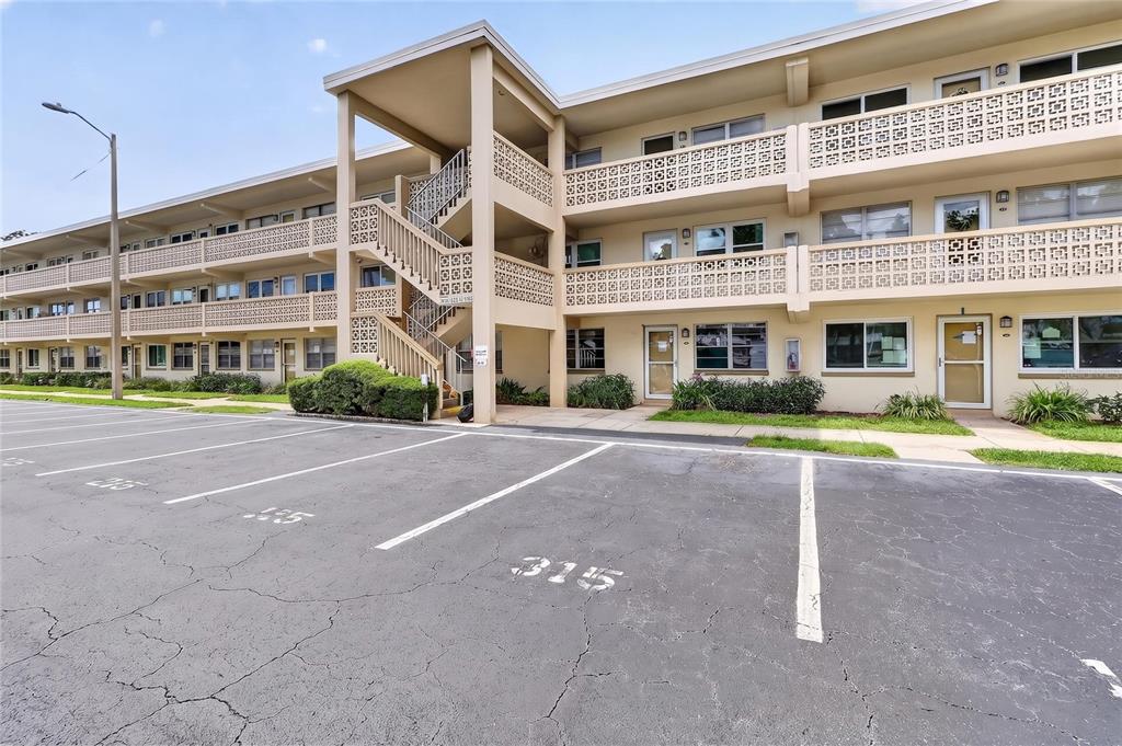 A multi-story apartment building features exterior staircases, concrete breezeways, and a paved parking lot — 951 79TH AVENUE N UNIT 115, ST PETERSBURG, FL