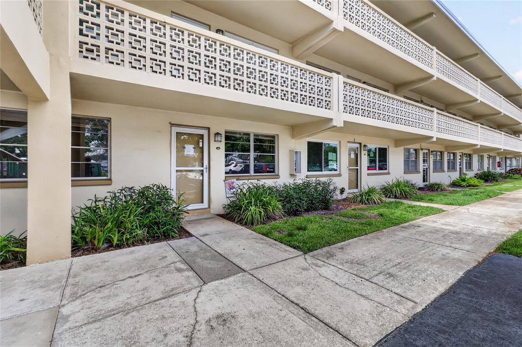 A multi-story apartment building exterior features concrete walkways, decorative breeze block railings, and landscaping — 951 79TH AVENUE N UNIT 115, ST PETERSBURG, FL