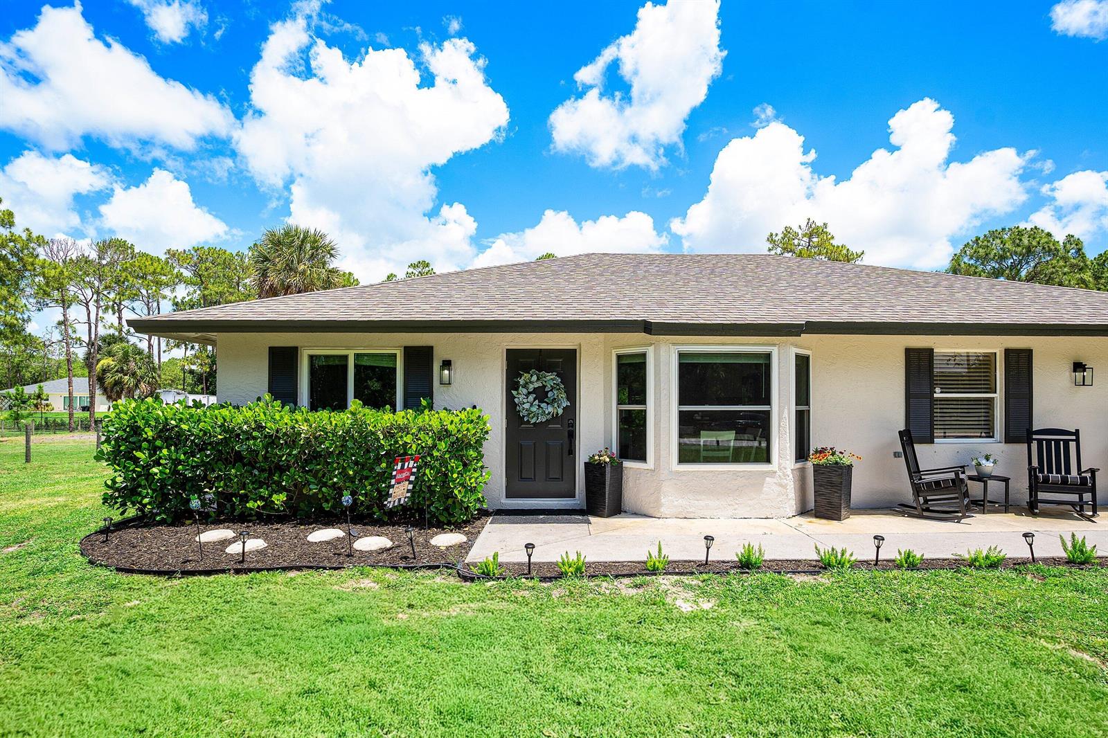 A single-story house with a dark front door, bay window, and a landscaped front yard — 17105 N 70th St Street N, FL 33470, FL