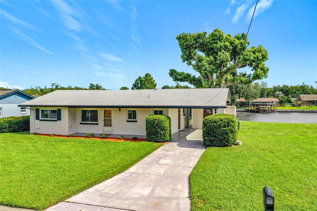 A single-story house with a carport and a lawn sits beside a canal — 13225 COUNTRY CLUB DRIVE, TAVARES, FL