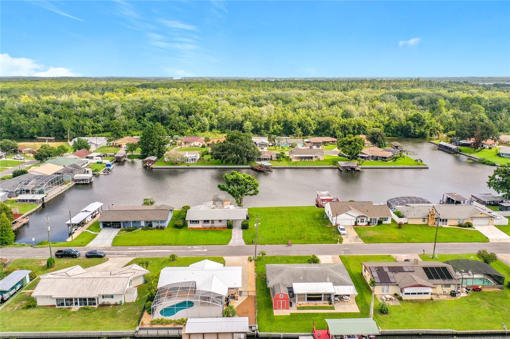 An aerial view shows waterfront houses with docks along a canal near a forest — 13225 COUNTRY CLUB DRIVE, TAVARES, FL