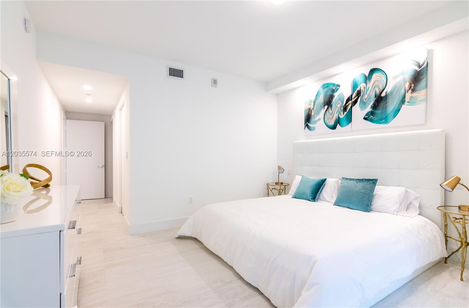 A modern bedroom features a white bed, teal accent pillows, and abstract wall art — 488 NE 18th St # 615, Miami FL 33132, MIAMI, FL