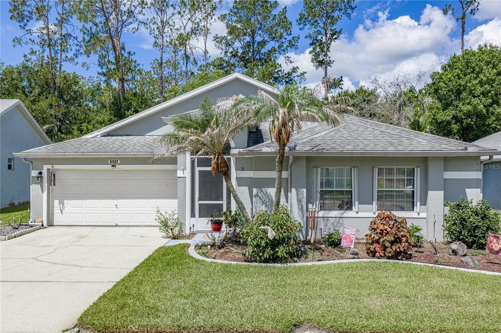 A single-story house with a gray exterior, a two-car garage, and a front yard — 5137 NEW BRITTANY LANE, ZEPHYRHILLS, FL