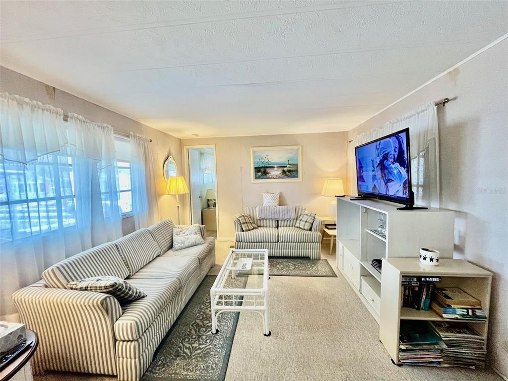 A living room features a striped sofa, a matching loveseat, and a television on a stand — 130 MELODY LANE, TARPON SPRINGS, FL