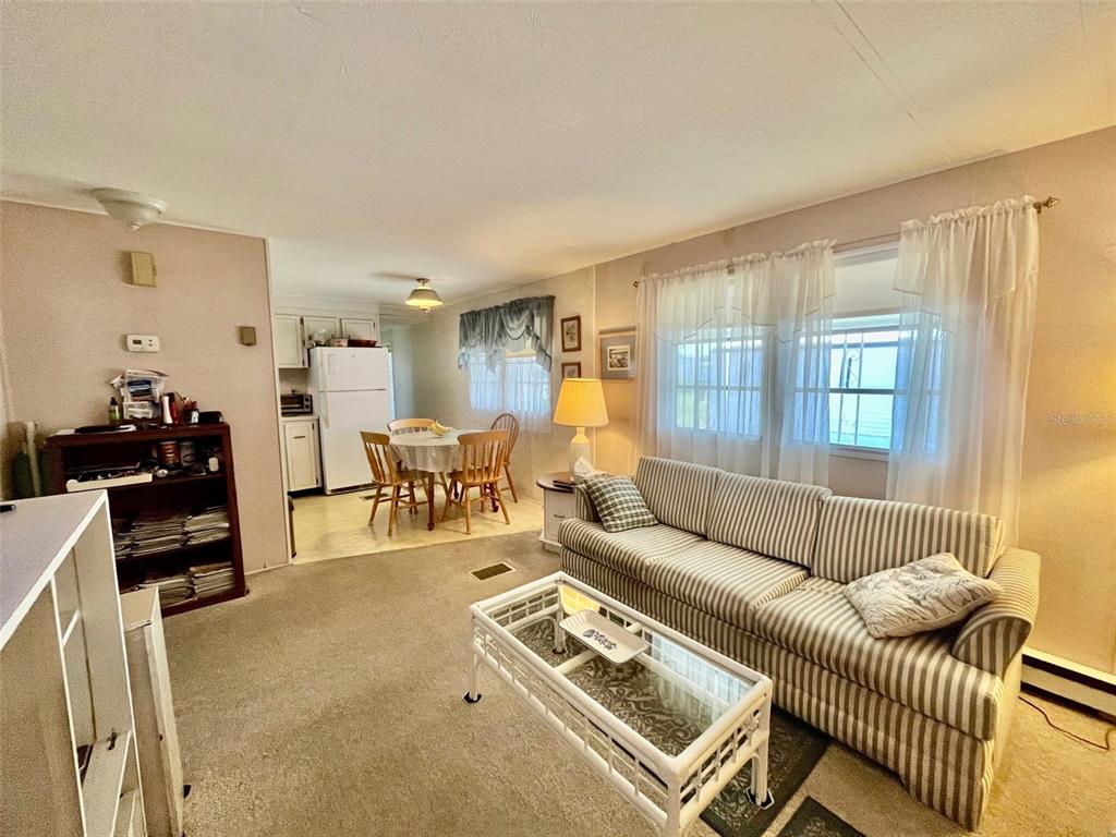 A living room with a striped sofa, glass coffee table, and an adjacent dining area — 130 MELODY LANE, TARPON SPRINGS, FL