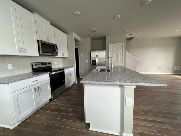 A kitchen features white cabinets, granite countertops, stainless steel appliances, and wood-look tile flooring — 756 LEGACY DR, DAVENPORT, FL