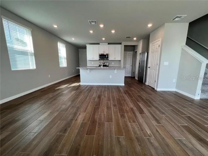 An open-concept kitchen features white cabinets, a central island, and wood-look tile flooring — 756 LEGACY DR, DAVENPORT, FL