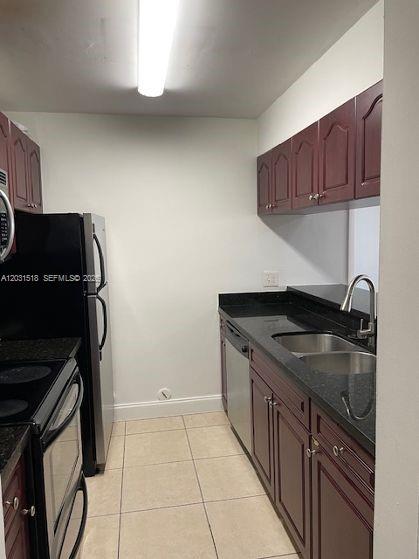 A galley kitchen features dark wood cabinets, black countertops, stainless steel appliances, and tile flooring — DORAL, FL