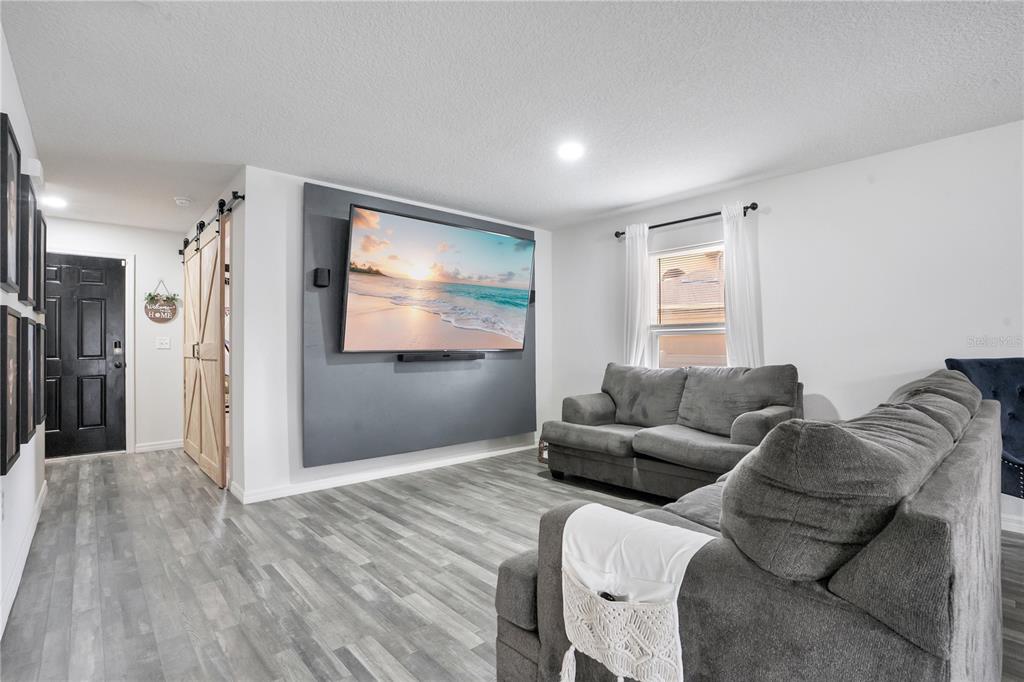 A living room features gray wood-look flooring, a wall-mounted television, and two gray sofas — 301 SALMON WAY, KISSIMMEE, FL