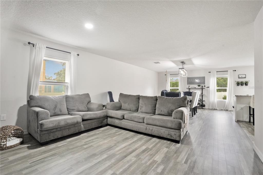 A living room with gray sectionals, wood-look tile flooring, and an adjacent dining area — 301 SALMON WAY, KISSIMMEE, FL