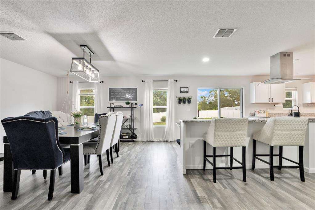 A dining area and kitchen with light wood-look flooring, white cabinets, and a kitchen island — 301 SALMON WAY, KISSIMMEE, FL