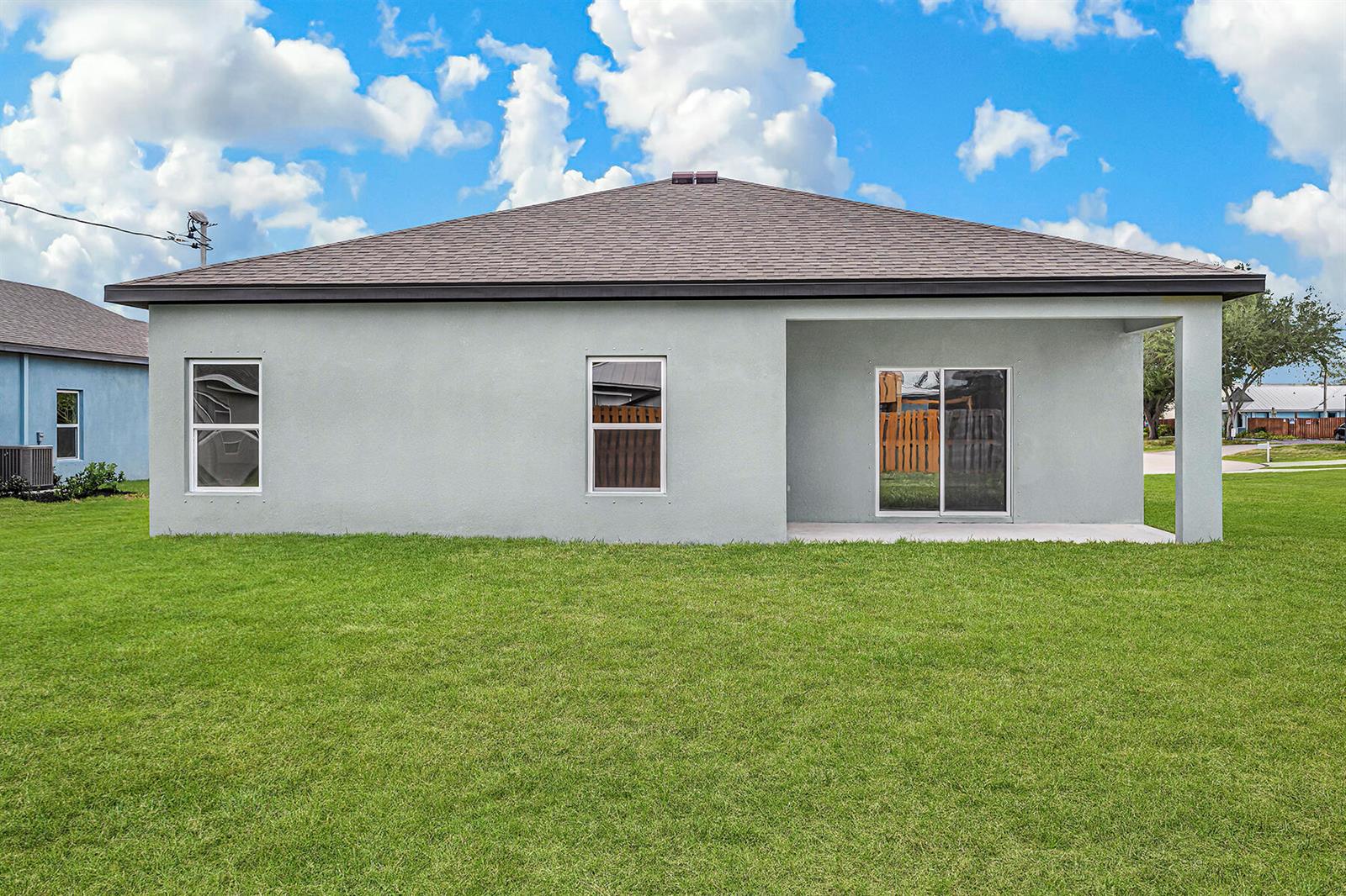 The rear exterior of a gray stucco house features a covered patio and lawn — 5701 Palm Drive, Fort Pierce FL 34982, FORT PIERCE, FL