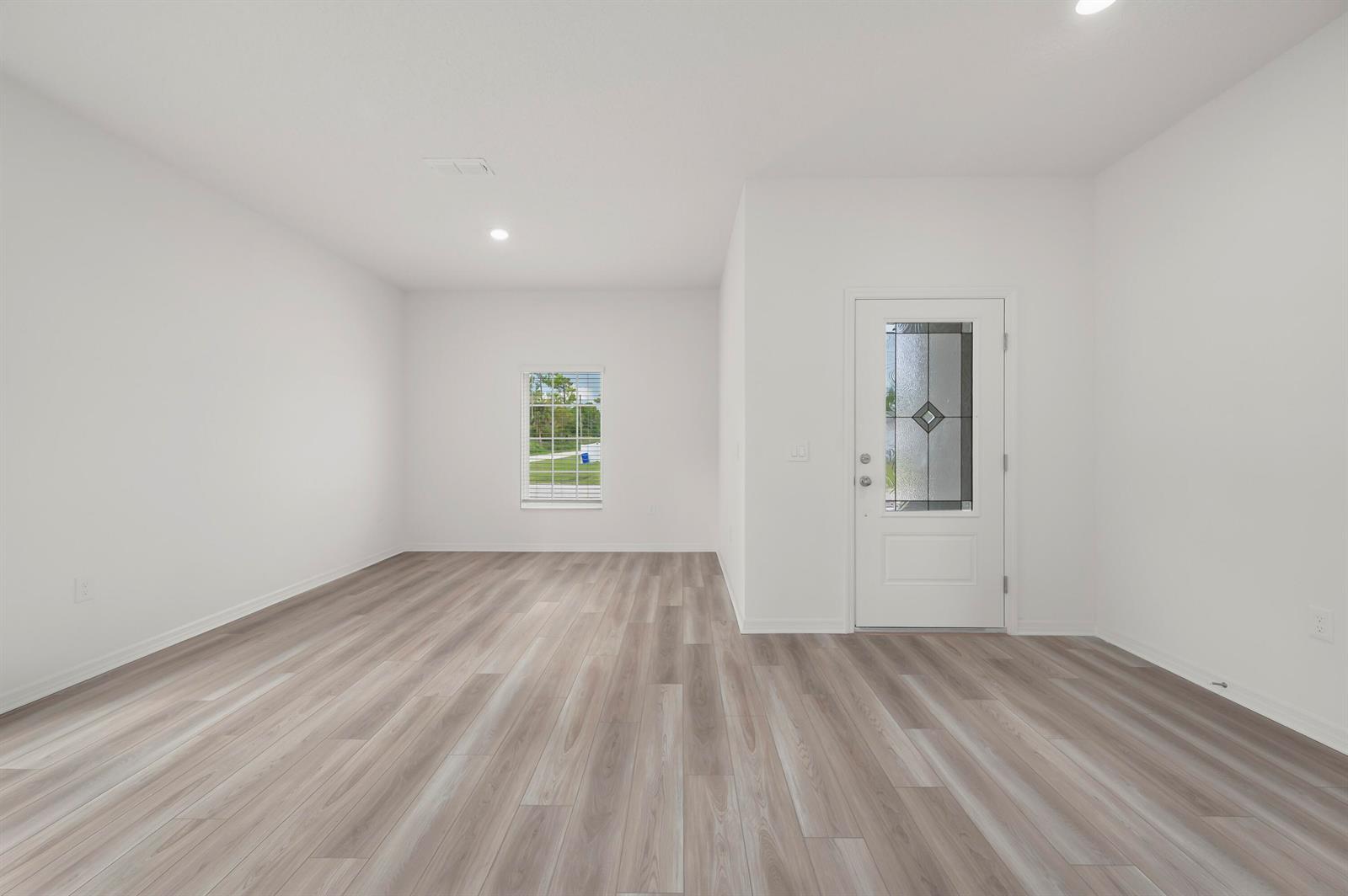 An empty room with white walls, light wood-look flooring, a single window, and an entry door — 5701 Palm Drive, Fort Pierce FL 34982, FORT PIERCE, FL