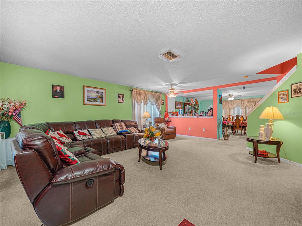 A living room features light green walls, a brown leather sectional, and beige carpeting — 7448 HUNTERS GREENE CIRCLE, LAKELAND, FL