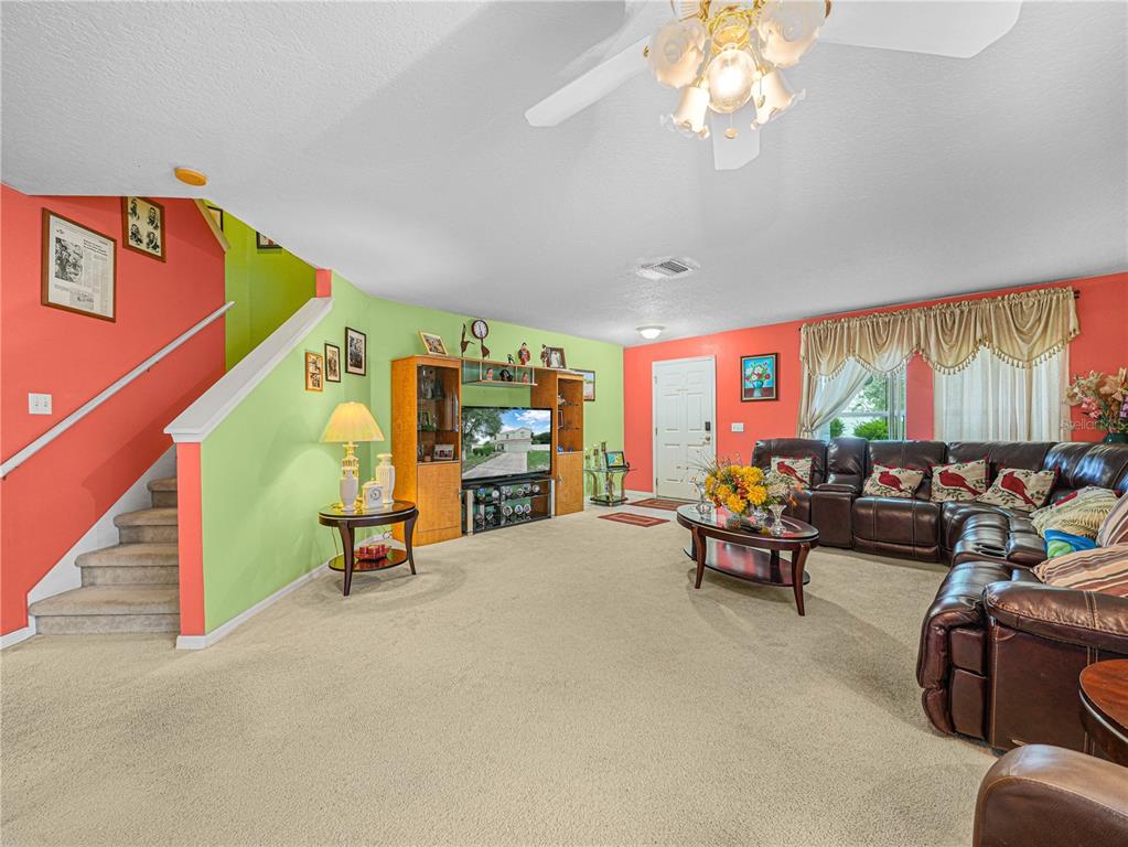 A living room features a staircase, a large entertainment center, and a brown leather sectional — 7448 HUNTERS GREENE CIRCLE, LAKELAND, FL