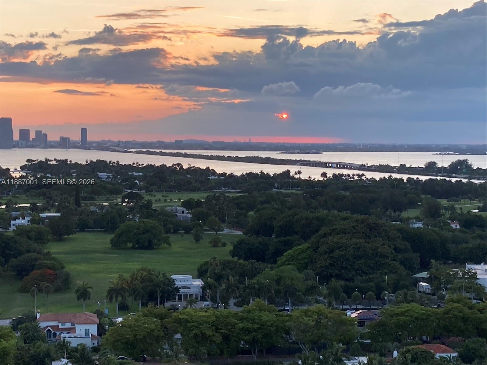 An elevated view of a lush green landscape, a bridge, and a sunset over water — 2555 Collins Ave # 2112, Miami Beach FL 33140, MIAMI BEACH, FL