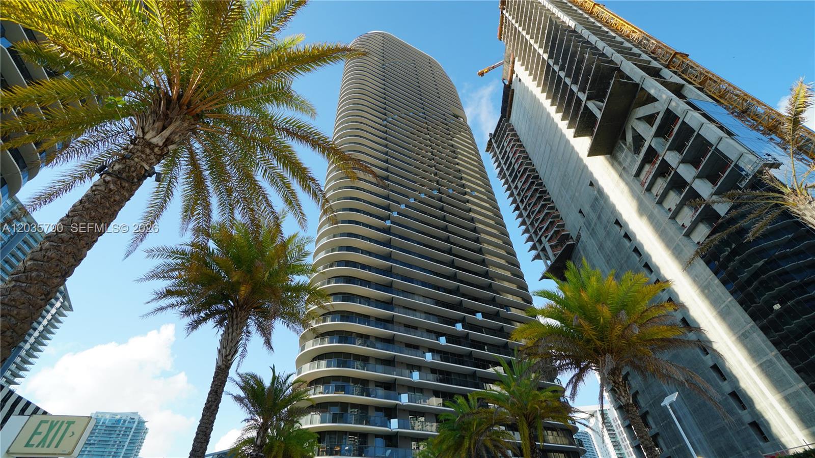 A low-angle view shows a tall, curved residential skyscraper next to a building under construction — 801 S Miami Ave # 2506, Miami FL 33130, MIAMI, FL