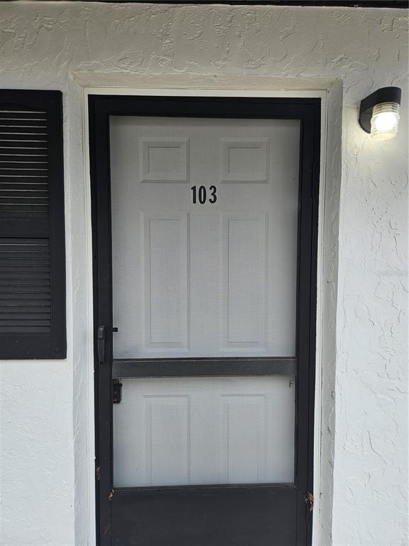 A white door with the number 103 and a black screen door on a white wall — 455 S BUCKMOORE ROAD UNIT 103, LAKE WALES, FL