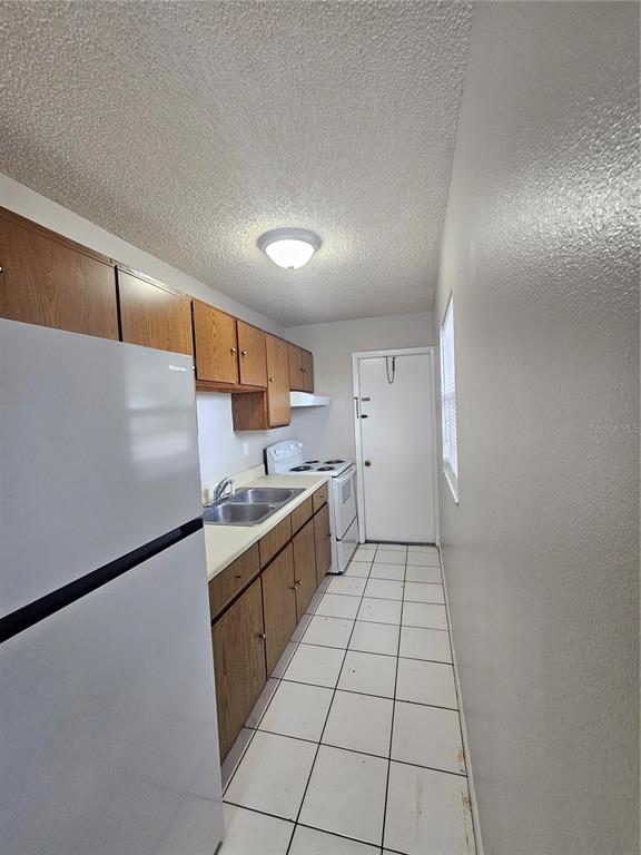 A galley kitchen features wood cabinets, white appliances, and white tile flooring — 455 S BUCKMOORE ROAD UNIT 103, LAKE WALES, FL