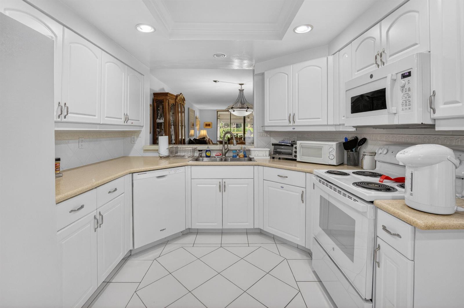 A white kitchen features light countertops, tile flooring, and a pass-through window to the living area — 15326 Strathearn Drive # 11902, Delray Beach FL 33446, DELRAY BEACH, FL