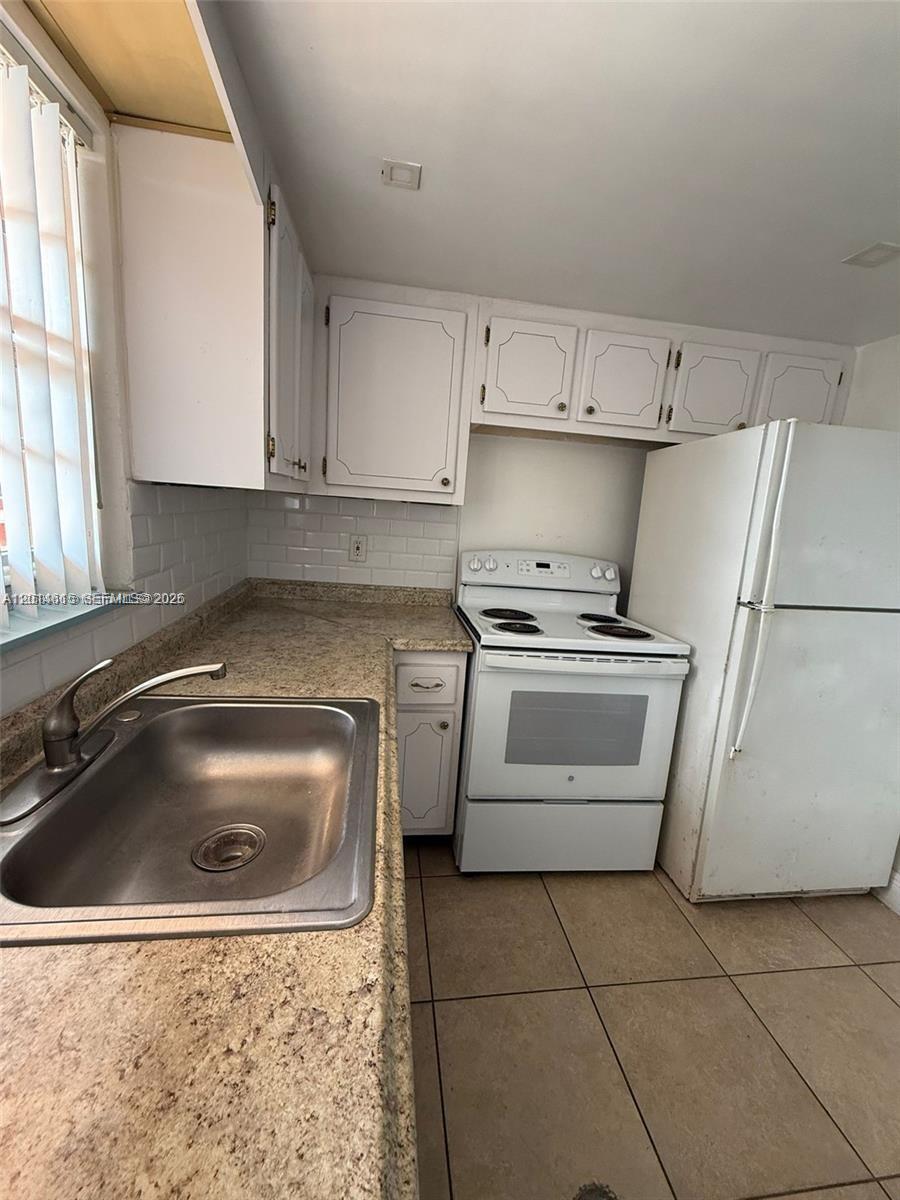A kitchen features white cabinets, a stainless steel sink, a white stove, and tile flooring — 18707 NE 2nd Ave # 918, Miami FL 33179, MIAMI, FL