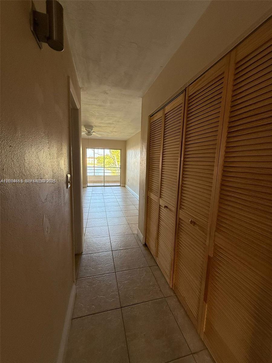 A hallway with beige tile flooring leads to a room with a sliding glass door — 18707 NE 2nd Ave # 918, Miami FL 33179, MIAMI, FL