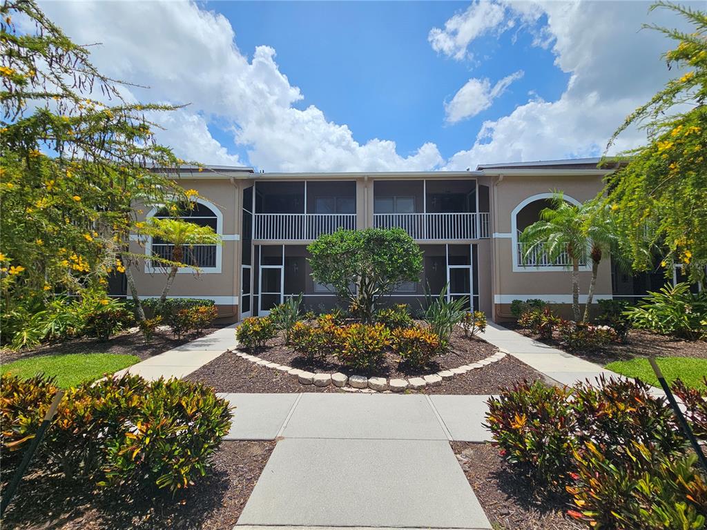 A two-story apartment building exterior features screened balconies, a landscaped courtyard, and concrete walkways — 5330 HYLAND HILLS AVENUE UNIT 2312, SARASOTA, FL