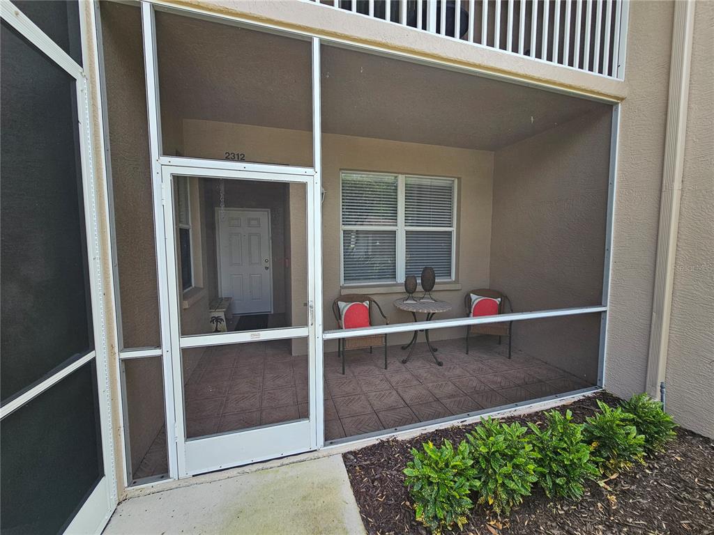 A screened-in patio features tiled flooring, two chairs, a small table, and an entryway door — 5330 HYLAND HILLS AVENUE UNIT 2312, SARASOTA, FL