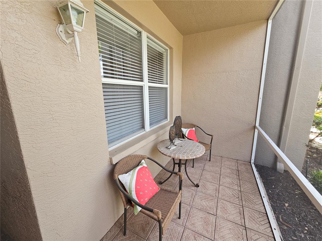 A covered patio features tiled flooring, two wicker chairs with watermelon pillows, and a small table — 5330 HYLAND HILLS AVENUE UNIT 2312, SARASOTA, FL