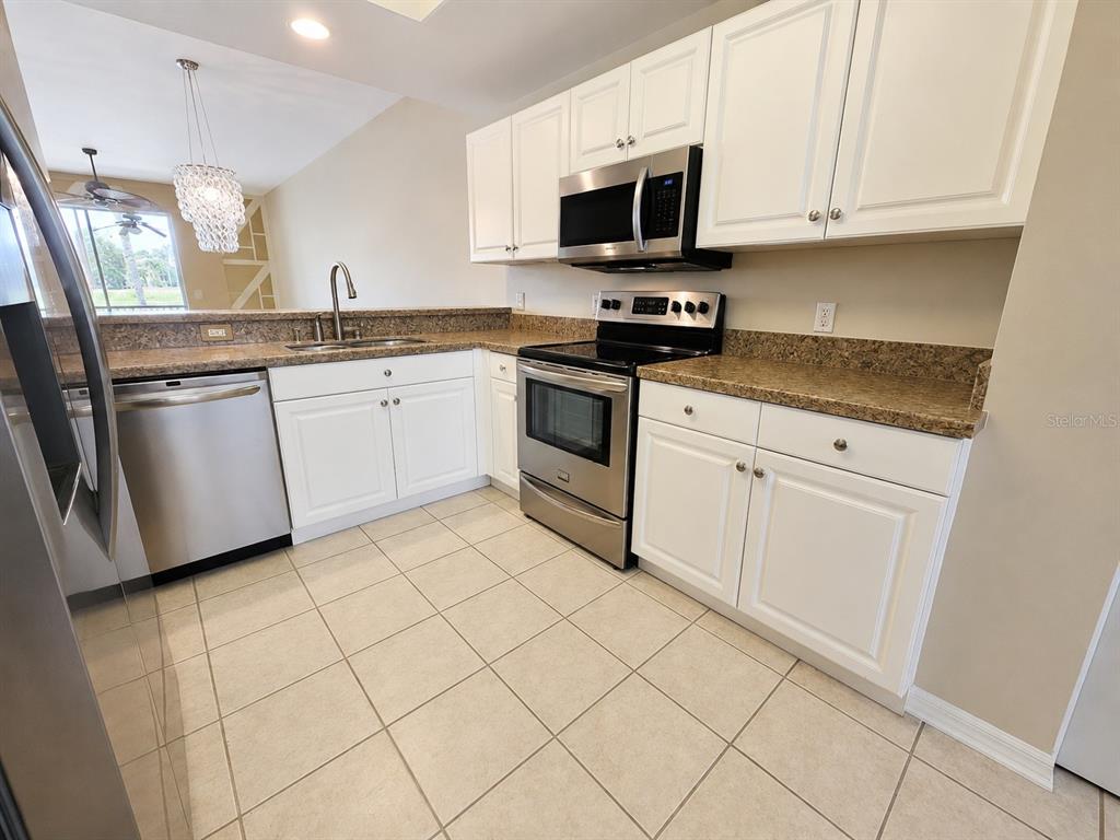 A kitchen features white cabinets, stainless steel appliances, and tan tile flooring — 5330 HYLAND HILLS AVENUE UNIT 2312, SARASOTA, FL