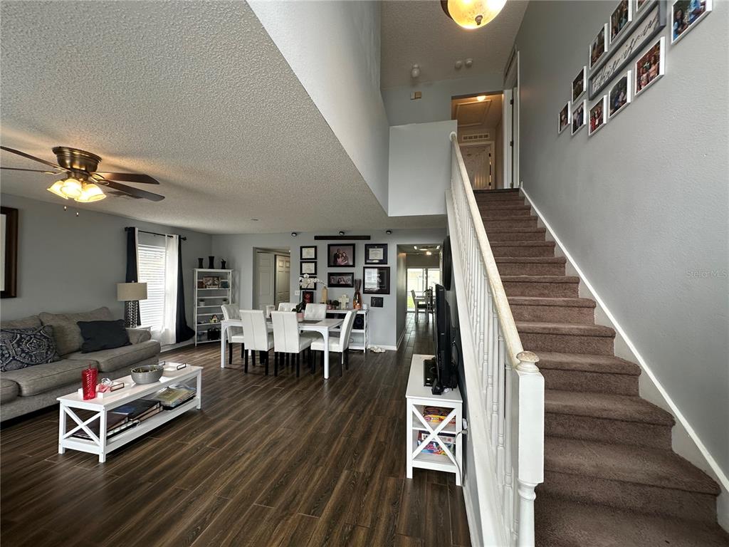 A living and dining area features wood-look flooring, a staircase, and a vaulted ceiling — 102 WHEATFIELD CIRCLE, SANFORD, FL