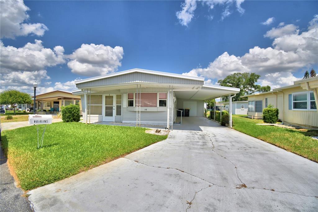 A single-story manufactured home features a front porch, a concrete driveway, and a carport — 118 PARADISE LANE, AUBURNDALE, FL